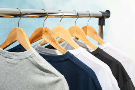 Rack with blank t-shirts on blue background, close upの写真素材