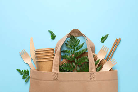 Eco bag with disposable tableware on blue background, space for text