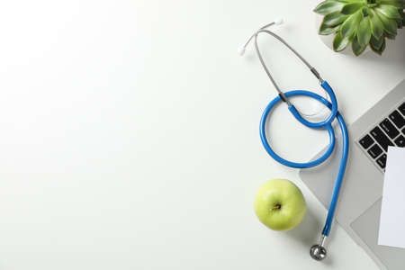 Stethoscope, apple, laptop and plant on white background, top view. Doctor workplaceの写真素材