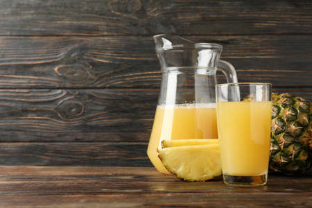 Pineapple, glass jug and glass with juice on wooden background, space for textの写真素材