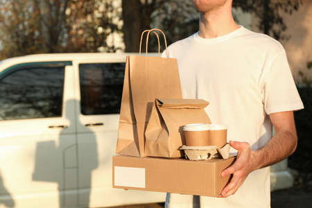 Ð¡ourier holds blank box, coffee cups and paper packages against car. Deliveryの写真素材