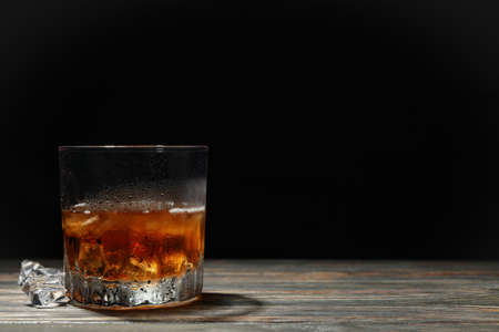 Glass of whiskey with ice cubes on wooden background, space for text