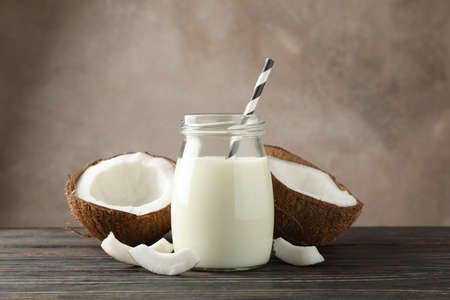 Bottle of coconut milk with straw, coconut and slice coconut on wooden background, space for textの写真素材