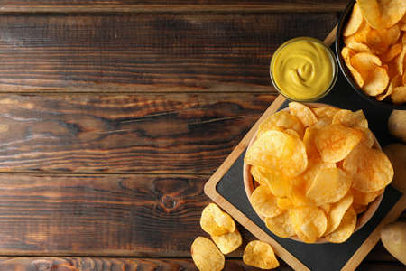 Potato chips. Beer snacks, sauce, potato on cutting board, on wooden background, space for text. Top viewの写真素材