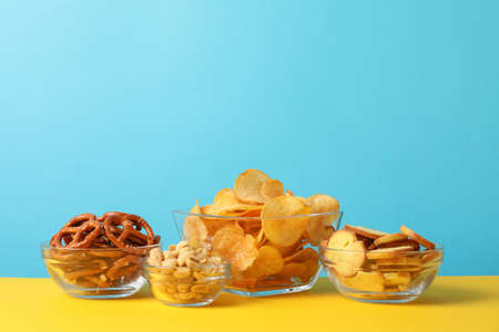 Beer snacks, potato chips, crackers in a bowl on yellow background against blue background, space for textの写真素材