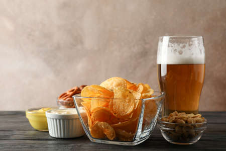 Beer snacks, glass of beer, potato chips, beer nuts, sauces, glass of beer on wooden background, space for textの写真素材