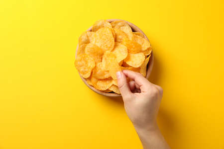 Hand holds potato chips on yellow background, space for text. Top view