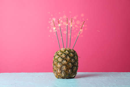 Pineapple with burning sparklers on blue table, space for textの写真素材