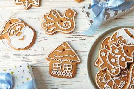 Flat lay composition with plate of Christmas cookies, gift boxes on white wooden background. Top...