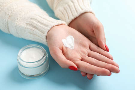 Woman hands, heart shape created from winter cream, jar of winter cream for skin on blue background....