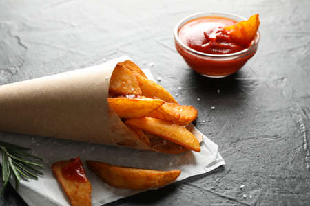 Baked potato wedges in package, red sauce on black background, space for text. Closeup