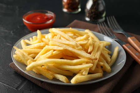 Plate of french fries, napkin, red sauce, forks on black background, space for text. Closeup