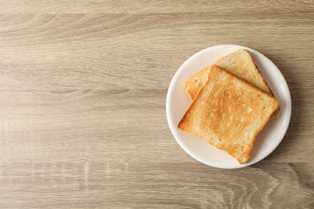 Plate with toasts on wooden background, top view