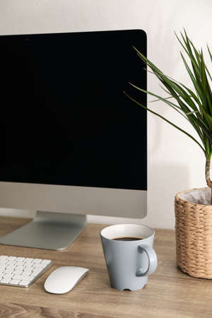 Workplace with computer, cup of coffee and plant on wooden table, close upの写真素材