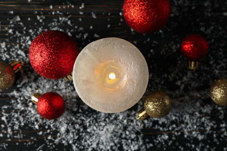 Burning candle and christmas balls on wooden background with snow, top viewの写真素材