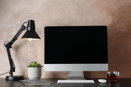 Workplace with computer and plant on wooden table. Light brown background
