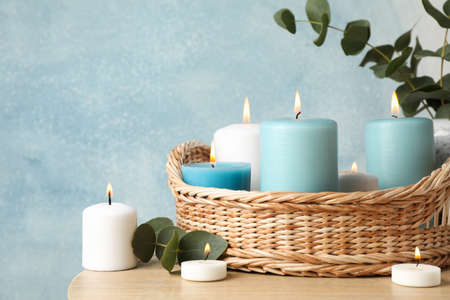 Burning candles, basket and vase with eucalyptus against blue background, close upの写真素材