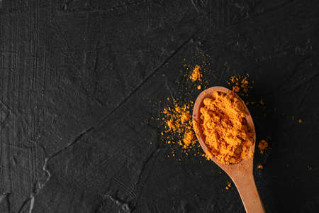 Wooden spoon with turmeric powder on black background, top viewの写真素材