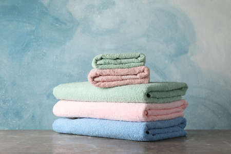 Stack of color towels on grey table against blue background, space for text