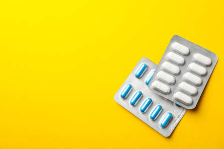 Pills in blister packs on yellow background, space for text