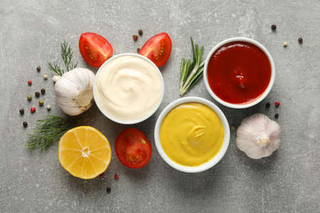 Set of different delicious sauces, garlic, cherry tomatoes on gray background, space for text. Top...