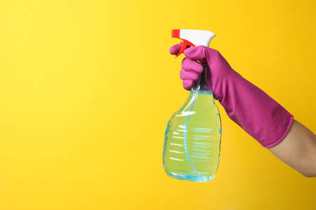 Hand in cleaning glove hold window cleaner on yellow background, space for text