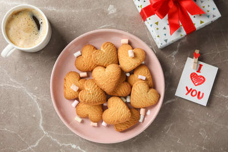 Plate with heart shaped cookies on decorated grey background, top view