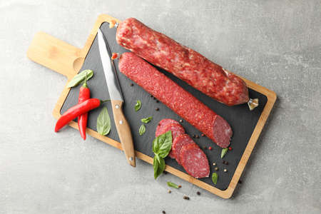 Cutting board with sausage, spice and knife on grey background, top view