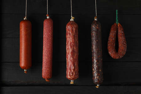 Delicious different hanging sausages on wooden background