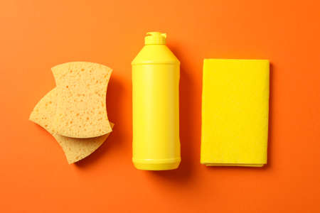 Flat lay with detergent and cleaning supplies on orange background, top view