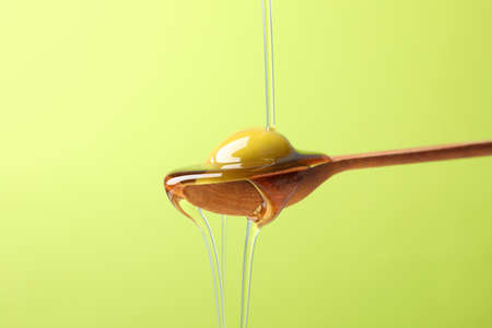 Wooden spoon with olive and pouring olive oil on green background, close upの写真素材