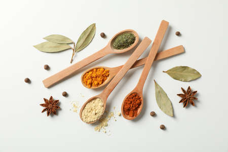 Spoons with different spices and ingredients on white background, top view