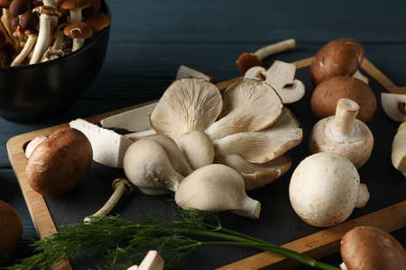 Different mushrooms, dill, bowl and board on wooden table, close upの写真素材