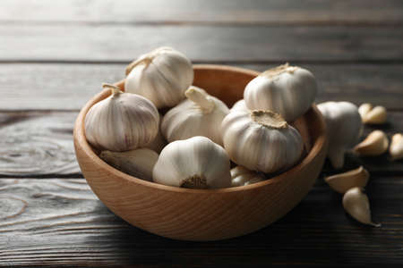 Wooden bowl of fresh garlic bulbs, slices on wooden background, top view. Closeupの写真素材