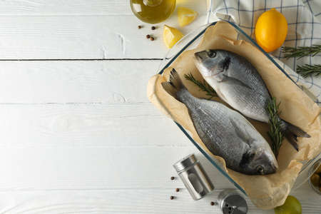 Baking tray with Dorado fishes and cooking ingredients on wood background, top viewの写真素材