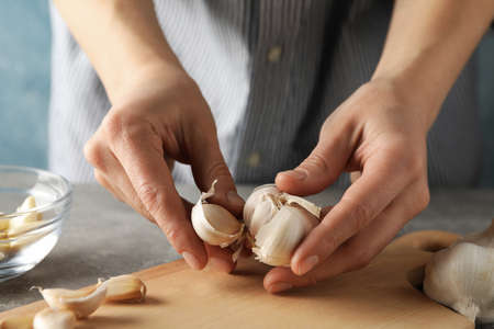 Women with garlic bulbs in her hands, bowl of garlic slices, board on grey wooden background. Closeupの写真素材