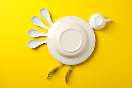 Bird made of plate and cutlery on yellow background, top view