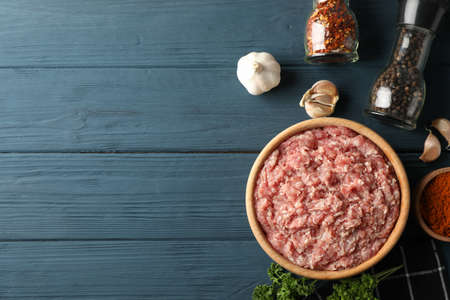 Spices and bowl with minced meat on wooden background, top view