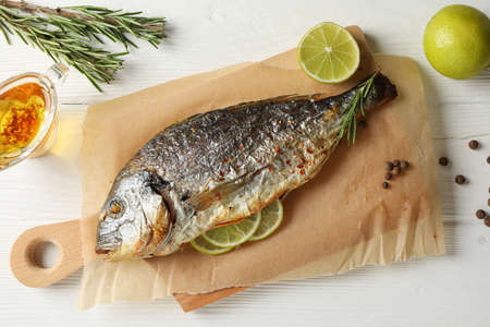 Baking paper with Dorado on garnished wooden background, top view