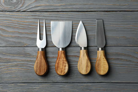 Cheese knives on wooden background, top view and space for text