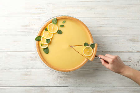 Lemon tart and person holding spatula with slice on wooden background, top viewの写真素材