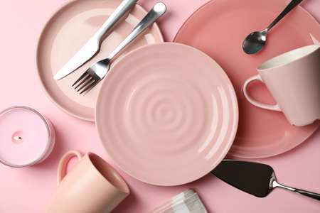 Tableware and cutlery on pink background, top view