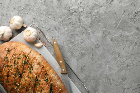 Garlic bread and knife on grey background, top view