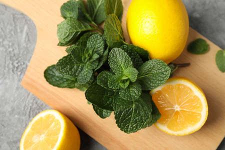 Cutting board with lemon and mint on grey background, close up
