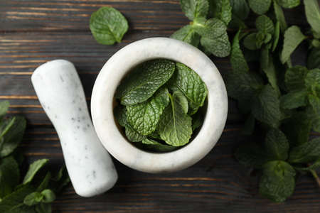 Mortar, pestle and mint on wooden background, top view