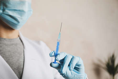 Doctor holds medical syringe of vaccine, injection on brown background. Coronavirus protection. Healthcare and medical conceptの写真素材