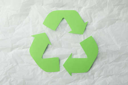 Recycling sign on white crumpled paper background, top view