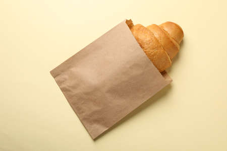 Craft paper bag with croissant on beige background, space for textの写真素材