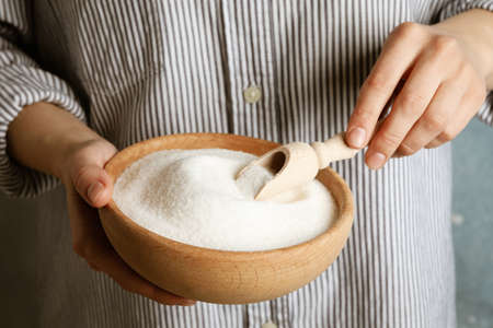 Woman holding bowl with sugar and scoop, close up