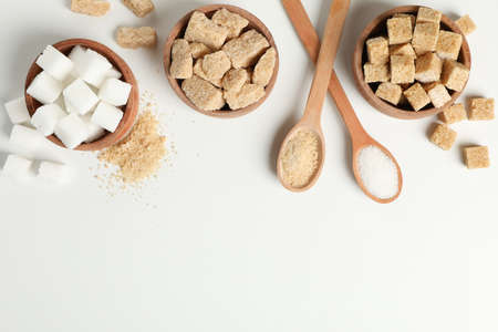 Bowls and spoons with sugar on white background, top view